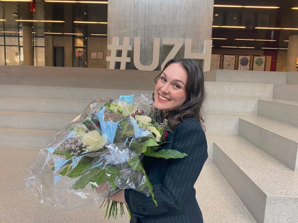 Dr. Donikë Sejdiu smiling and holding flowers at UZH